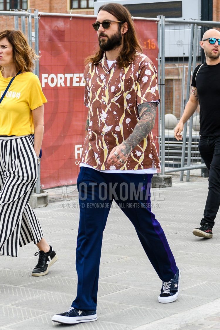 A spring/summer men's coordinate outfit with plain sunglasses, brown other shirt, plain white t-shirt, plain navy sidelined pants, and navy low-cut sneakers.
