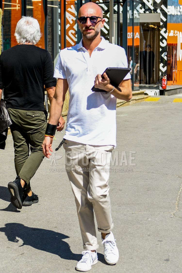 A summer men's coordinate outfit with plain sunglasses, a plain white polo shirt, plain beige chinos, and white low-cut sneakers.