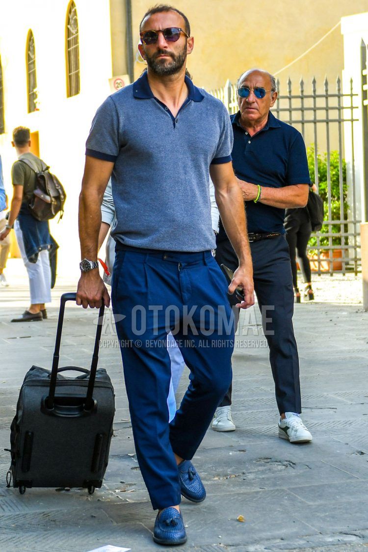 Summer men's coordinate outfit with black/brown tortoiseshell sunglasses, plain blue/navy polo shirt, plain navy pleated pants, slacks, and navy tassel loafer leather shoes.