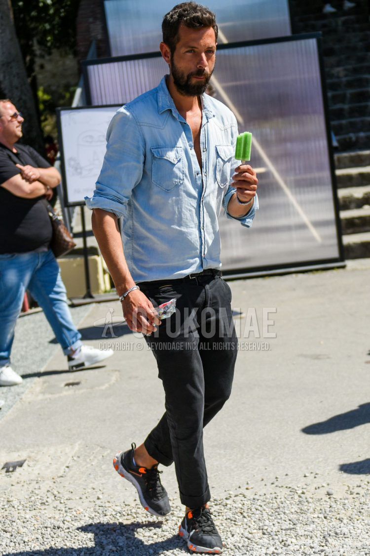 A light blue solid denim/chambray shirt, solid black leather belt, solid black denim/jeans, and Nike React Element 55 black low-cut sneakers for men's spring/summer outfits.