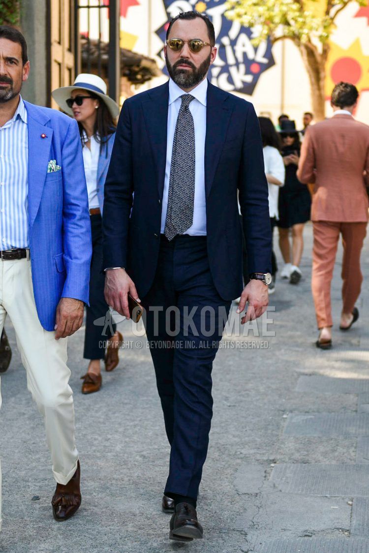 Spring, summer and fall men's coordinate outfit with clear plain sunglasses, plain white shirt, plain black socks, black and other loafer leather shoes, plain navy suit and gray and other tie.