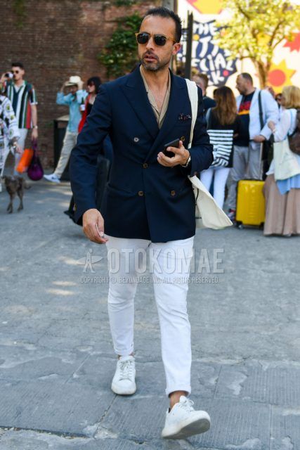Spring, summer and fall men's coordinate outfit with solid beige sunglasses, solid navy tailored jacket, open collar solid beige shirt, solid white cotton pants and white low-cut sneakers.