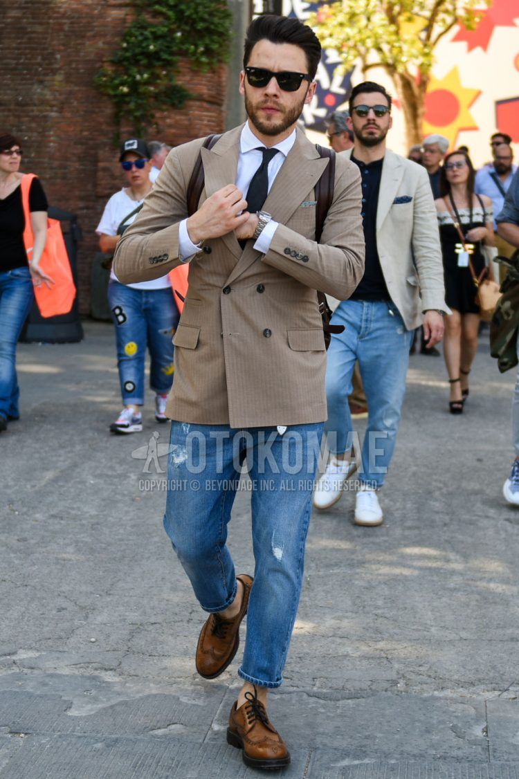 A spring and fall men's outfit with plain black Wellington Ray-Ban Wayfarer sunglasses, beige striped tailored jacket, plain white shirt, plain blue damaged jeans, brown wingtip leather shoes, and plain black tie.