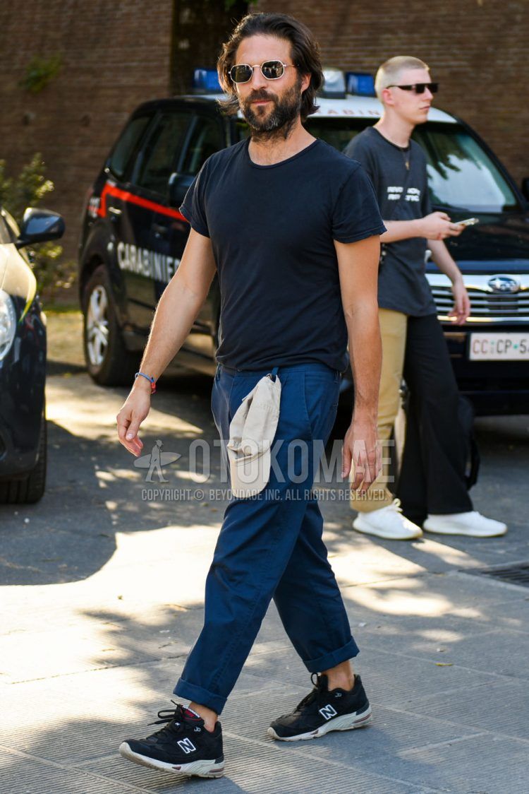 A summer men's coordinate outfit with plain black/gold sunglasses, plain black t-shirt, plain navy chinos, and New Balance 991 black low-cut sneakers.