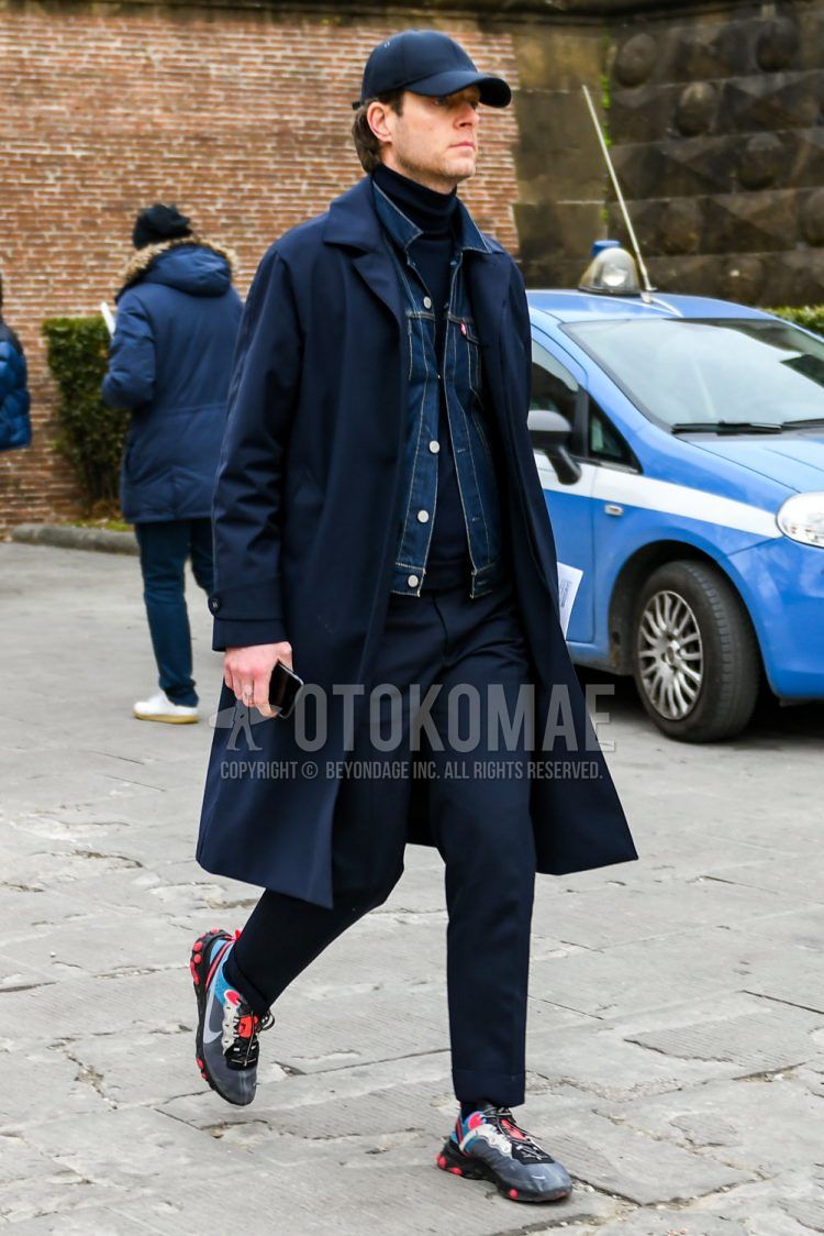 A men's fall/winter outfit with a solid navy baseball cap, solid navy stainless steel collar coat, solid blue denim jacket, solid navy turtleneck knit, solid navy slacks, and Nike gray low-cut sneakers.