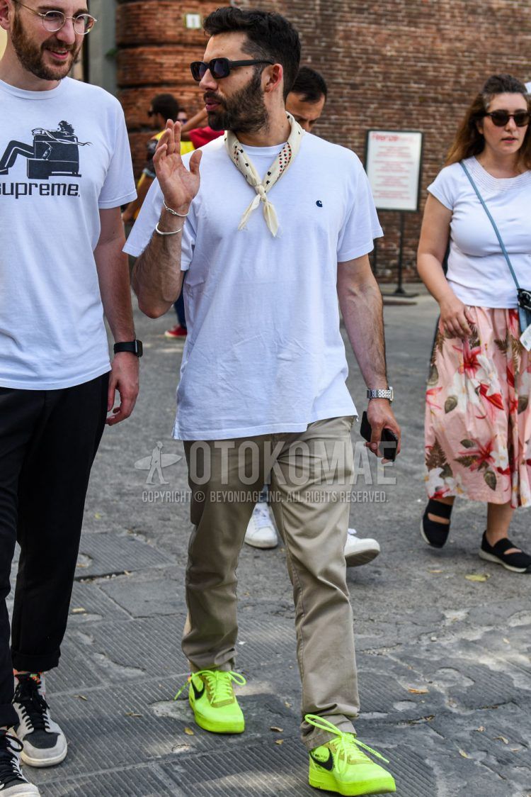 A summer men's coordinate outfit with solid black sunglasses, solid beige bandana/neckerchief, solid white t-shirt, solid beige cotton pants, and Nike yellow low-cut sneakers.