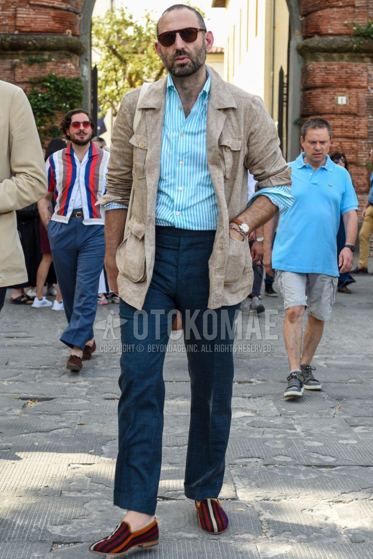Spring and summer men's coordinate outfit with plain brown sunglasses, plain linen beige safari jacket, light blue striped shirt, plain gray slacks, plain beltless pants, and multi-colored other loafer leather shoes.