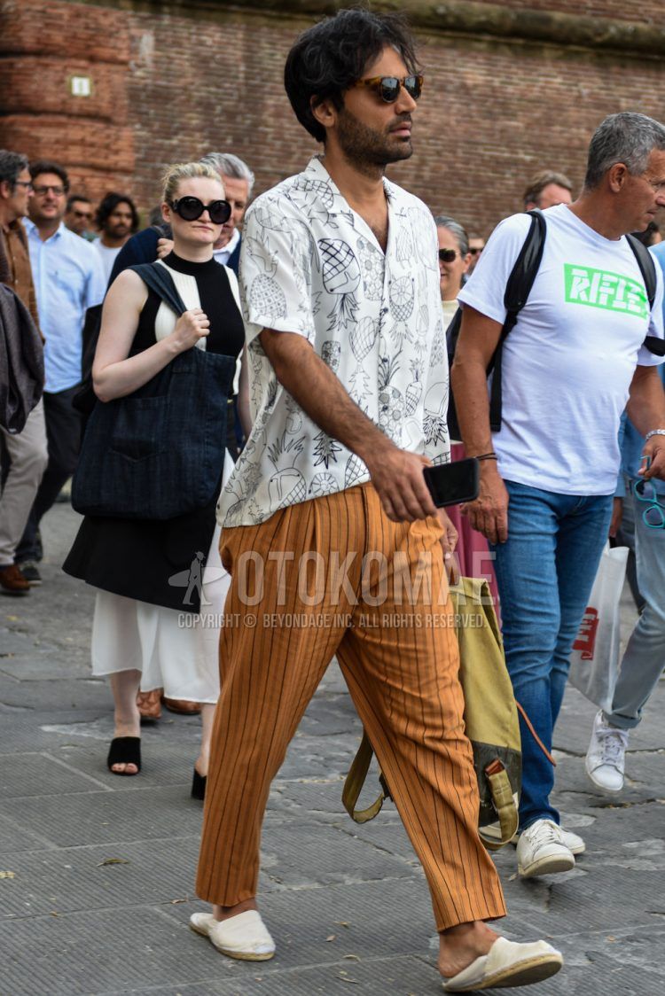 A summer men's outfit with Wellington brown tortoiseshell sunglasses, short sleeve open collar white other shirt, beige striped slacks, and plain white espadrilles.