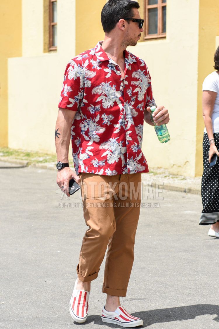 Summer men's coordinate outfit with plain black sunglasses, red botanical shirt, plain brown cotton pants, and open-collar red slip-on sneakers.