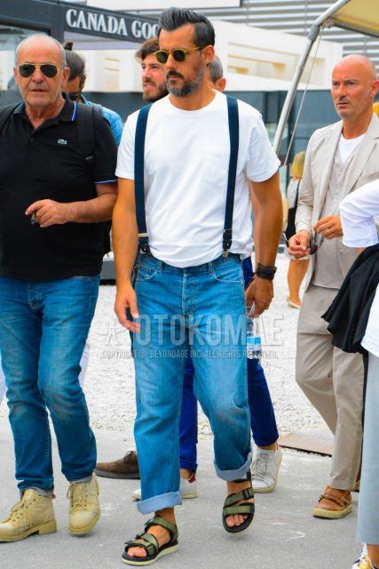 A spring/summer men's coordinate outfit with solid color sunglasses, solid color t-shirt, solid color suspenders, solid color blue denim/jeans, and sports sandals.