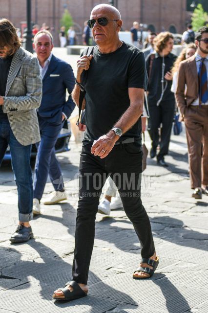 A summer men's coordinate outfit with solid black sunglasses, solid black t-shirt, solid gray mesh belt, solid black denim/jeans, and black leather sandals.