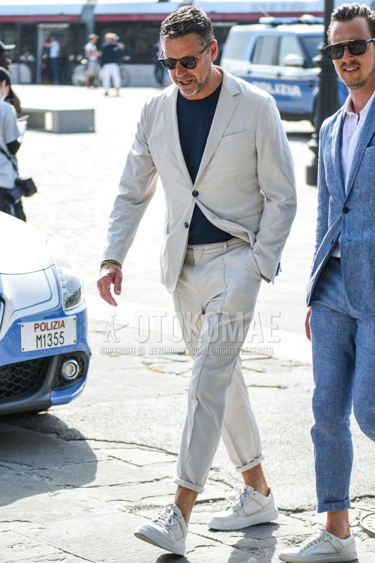 A spring and fall men's coordinate outfit with plain black sunglasses, plain navy t-shirt, white low-cut sneakers, and plain white suit.