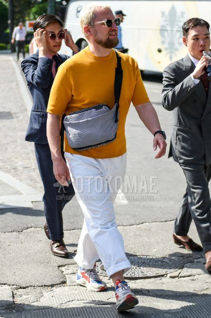 A summer men's coordinate outfit with clear solid color sunglasses, solid color orange sweater, solid color white wide pants, multi-colored low-cut sneakers, and solid color gray body bag.