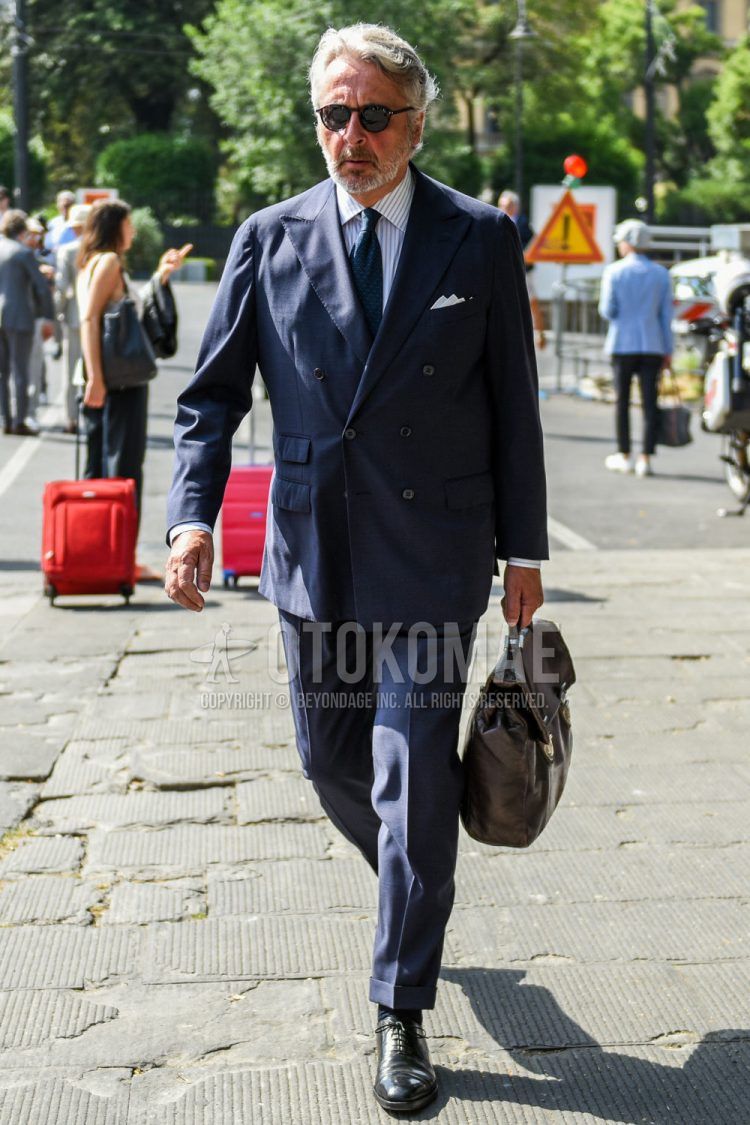 A spring/fall men's outfit with plain black sunglasses, white striped shirt, plain navy socks, plain black plain toe leather shoes, plain brown briefcase/handbag, plain navy suit, and plain navy tie.