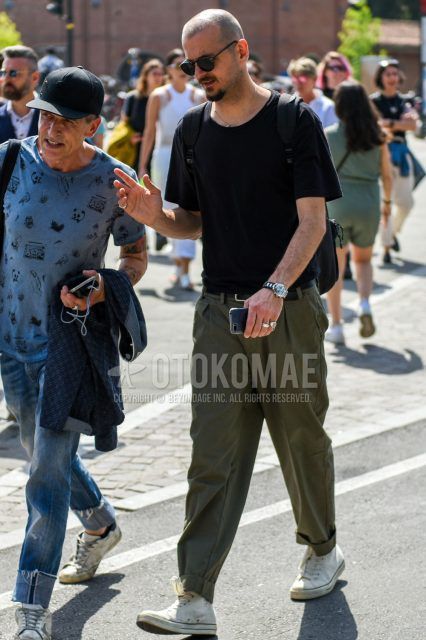 A summer men's coordinate outfit with plain black sunglasses, a plain black T-shirt, plain olive green wide-leg pants, and white high-cut Converse sneakers.
