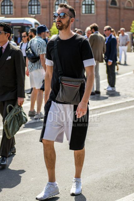 A summer men's coordinate outfit with plain black sunglasses, plain black t-shirt, plain black/white shorts, Nike white low-cut sneakers, and a dark gray plain shoulder bag.