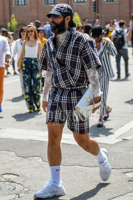 Spring/summer men's coordinate outfit with multi-colored checked baseball cap, multi-colored checked others, multi-colored checked shorts, Nike plain white socks, Nike white low-cut sneakers, and plain white clutch/second bag/drawstring bag.