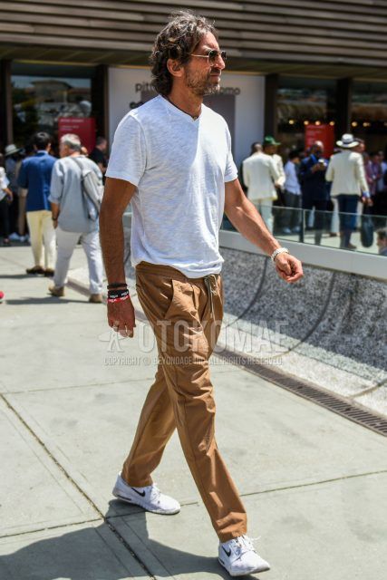 A summer men's coordinate outfit with plain gold sunglasses, plain white t-shirt, plain brown easy pants, and white low-cut Nike sneakers.