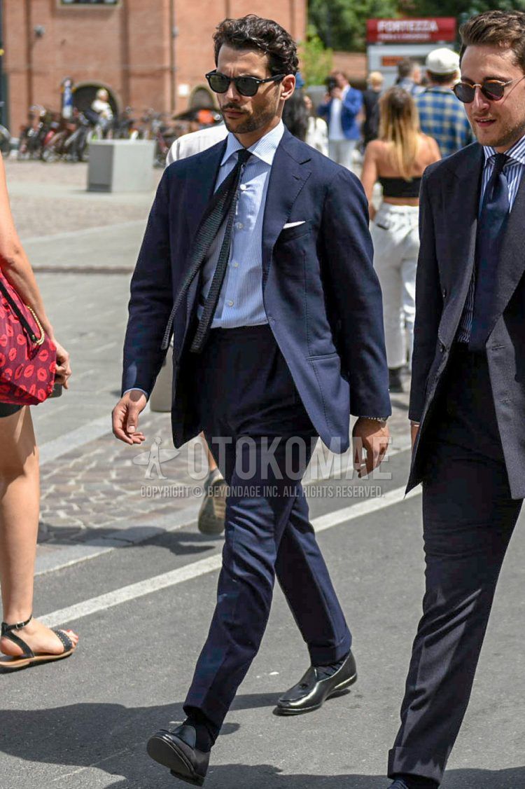 A spring and fall men's coordinate outfit with plain black sunglasses, plain white shirt, black other loafer leather shoes, plain navy suit, and plain navy knit tie.
