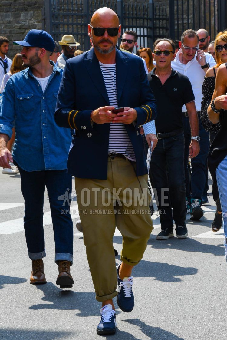 A spring/summer/fall men's coordinate outfit with plain sunglasses, plain navy tailored jacket, white striped t-shirt, plain beige chinos, and Nike blue low-cut sneakers.