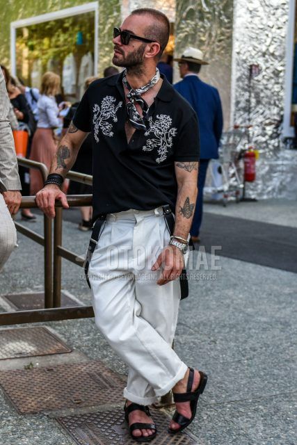 Summer men's coordinate outfit with plain black sunglasses, plain black scarf/stall, black graphic polo shirt, plain white wide-leg pants, and black leather sandals.