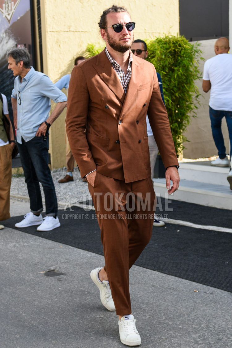 A spring and fall men's outfit with plain sunglasses, a brown checked shirt, Diadora white low-cut sneakers, and a plain brown suit.