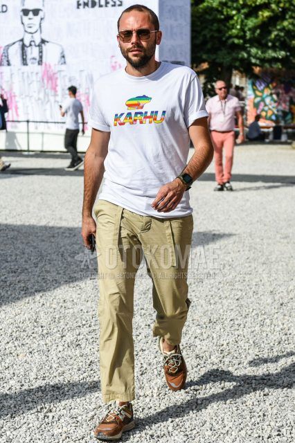 A summer men's coordinate outfit with plain sunglasses, a white graphic t-shirt, plain beige cotton pants, and brown low-cut sneakers.