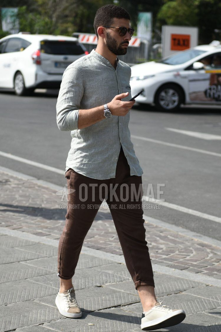 Summer men's coordinate outfit with brown tortoiseshell sunglasses, band collar linen gray striped shirt, plain brown chinos, and beige/brown low-cut sneakers.