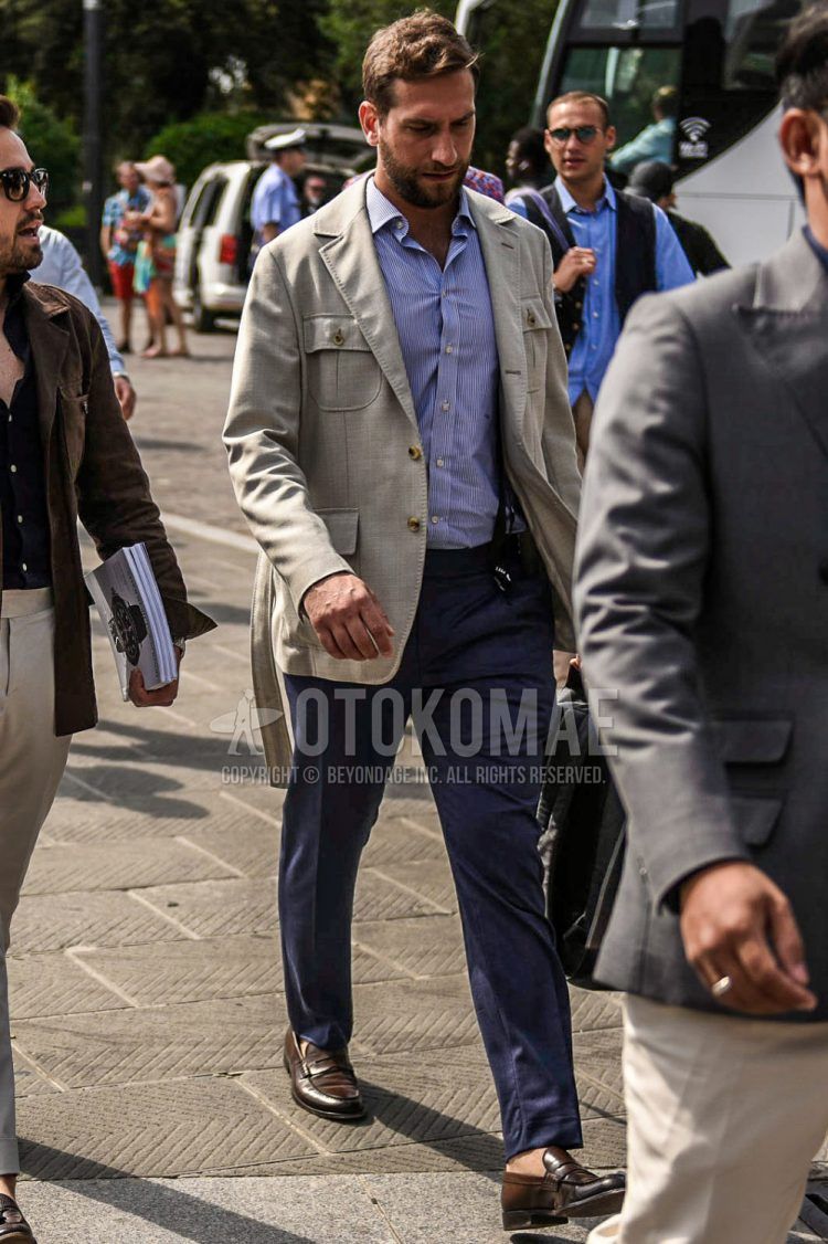 Spring and fall men's coordinate outfit with solid beige safari jacket, light blue striped shirt, solid black suspenders, solid gray slacks, and brown coin loafer leather shoes.