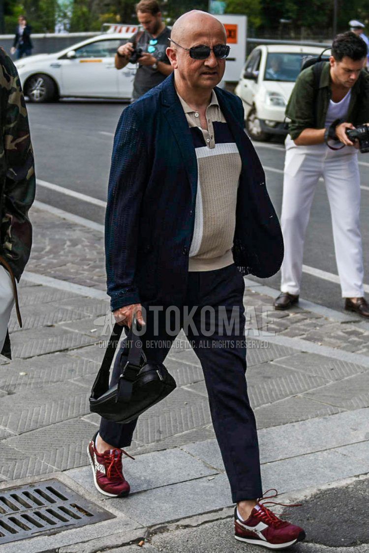 Spring, summer and fall men's coordinate outfit with plain black sunglasses, plain navy tailored jacket, plain beige polo shirt, plain gray slacks and red low-cut sneakers by Diadora.