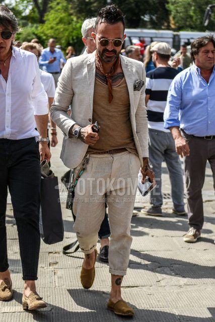 A summer men's outfit with plain black/gold sunglasses, beige/brown and other bandana/neckerchief, plain beige t-shirt, plain brown leather belt, plain beige espadrilles, and plain beige suit.
