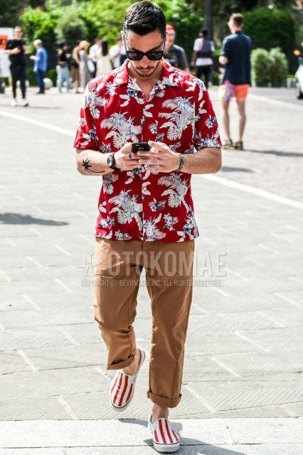 Summer men's coordinate outfit with plain black sunglasses, short sleeve open collar red botanical shirt, plain beige/brown cargo pants, and white/red slip-on sneakers.