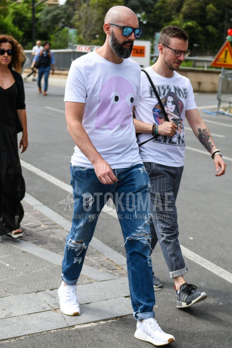 A summer men's coordinate outfit with gray other sunglasses, white graphic t-shirt, plain blue damaged jeans, and Adidas NMD white low-cut sneakers.