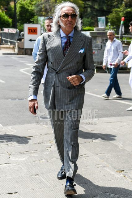 Spring, summer and fall men's coordinate outfit with round beige tortoiseshell sunglasses, solid light blue shirt, solid blue socks, black tassel loafer leather shoes, gray striped suit and red other tie.