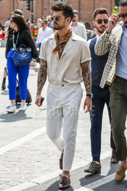 Summer men's coordinate outfit with round gold/black solid sunglasses, beige other bandana/neckerchief, short sleeve open collar solid beige shirt, solid white slacks, brown tassel loafer leather shoes.