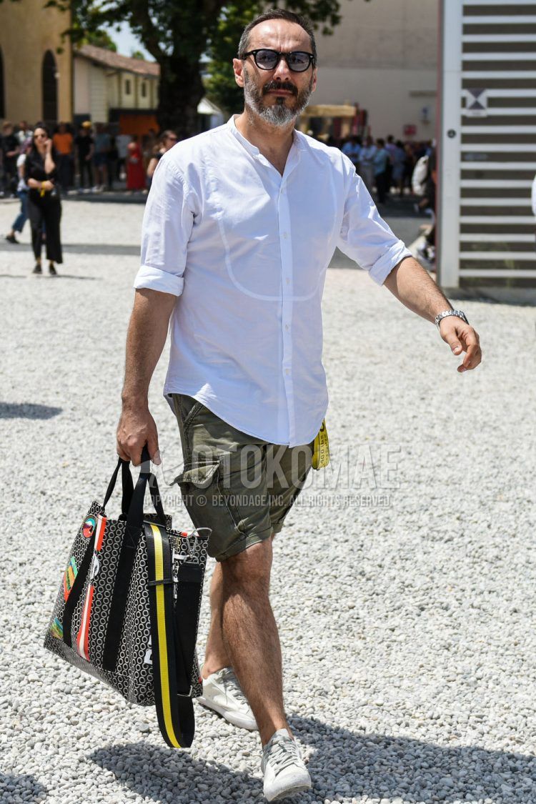 A summer men's outfit with plain black sunglasses, plain white shirt, off-white yellow graphic tape belt, plain olive green shorts, plain cargo pants, white low-cut sneakers, and black other briefcase/handbag.