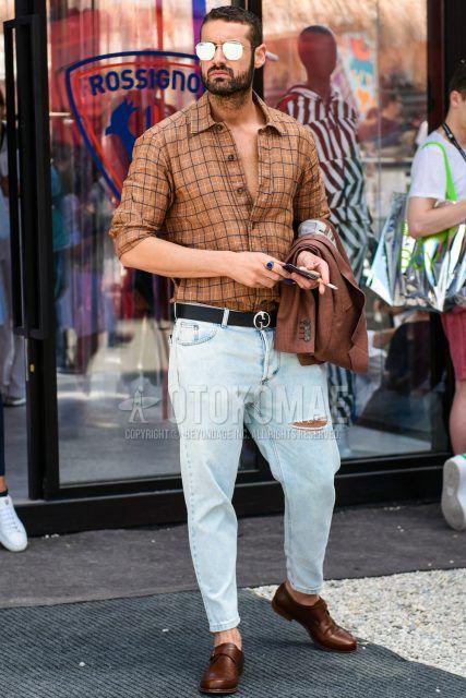 A spring/summer men's coordinate outfit with plain gold/silver sunglasses, brown checked shirt, plain black leather belt, plain light blue damaged jeans, and brown monk shoe leather shoes.