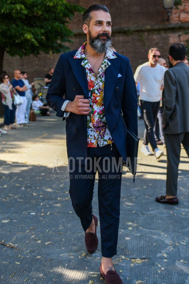 Spring/Summer/Fall men's coordinate outfit with open collar multi-colored botanical shirt, brown other loafer leather shoes, navy solid color clutch bag/second bag/drawstring, and navy solid color suit.
