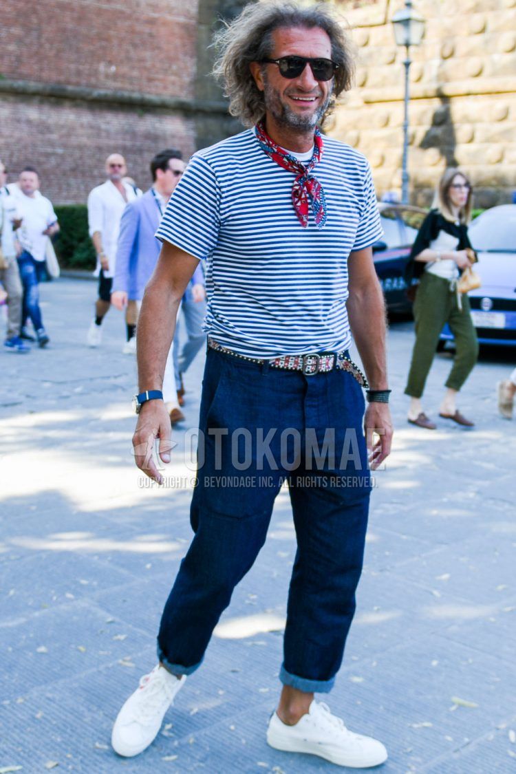 A summer men's outfit of plain black Tom Ford sunglasses, red and other bandana/neckerchief, navy and white striped t-shirt, multi-colored and other leather belt, plain navy denim/jeans, and white low-cut sneakers.