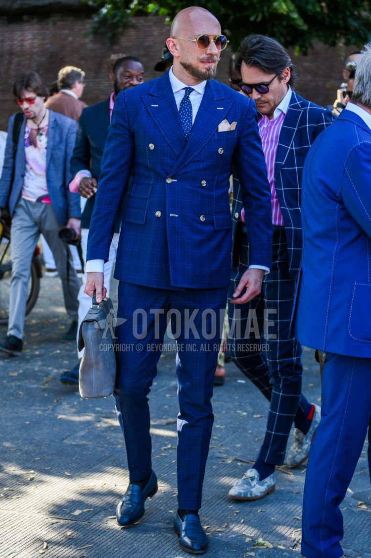 A men's spring/summer/fall outfit with plain gold sunglasses, plain white shirt, plain navy socks, navy coin loafer leather shoes, plain gray briefcase/handbag, navy check suit, and blue dot tie.
