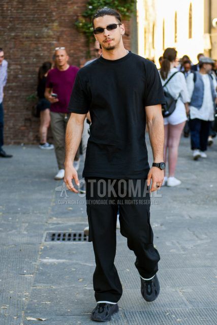 A summer men's coordinate outfit with plain black sunglasses, a plain black t-shirt, plain black wide-leg pants, and black low-cut Adidas sneakers.