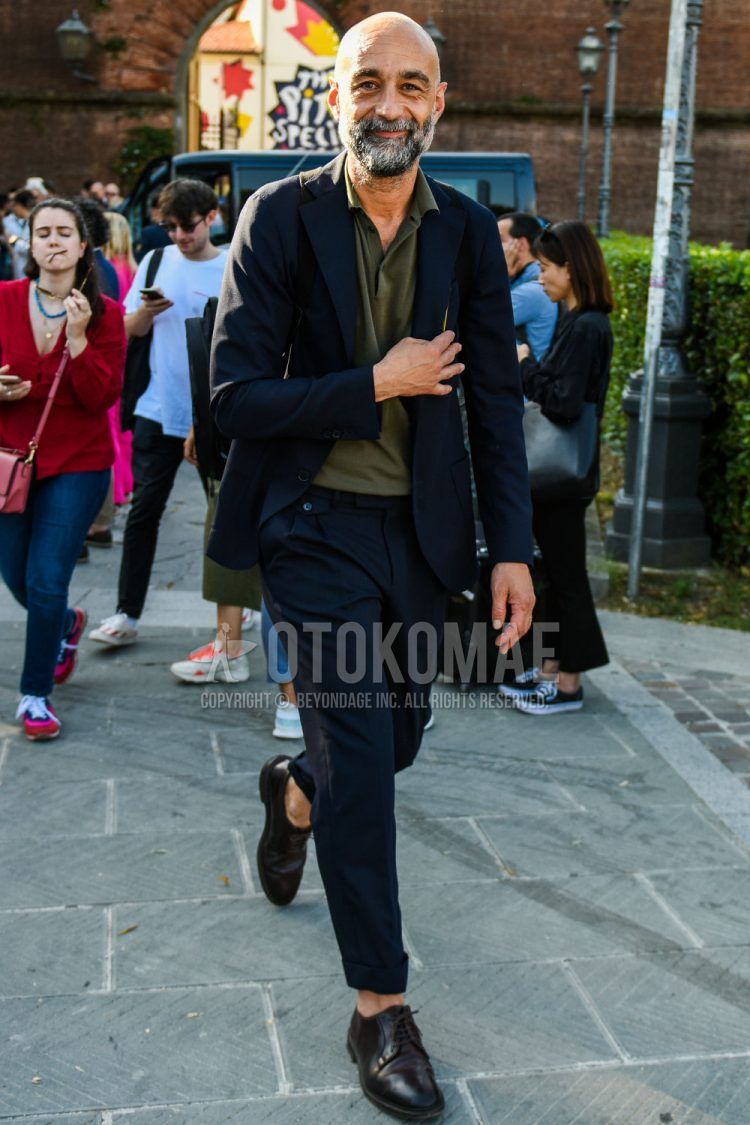 Spring, summer, and fall men's coordinate outfit with olive green solid polo shirt, brown plain-toe leather shoes, and solid black suit.