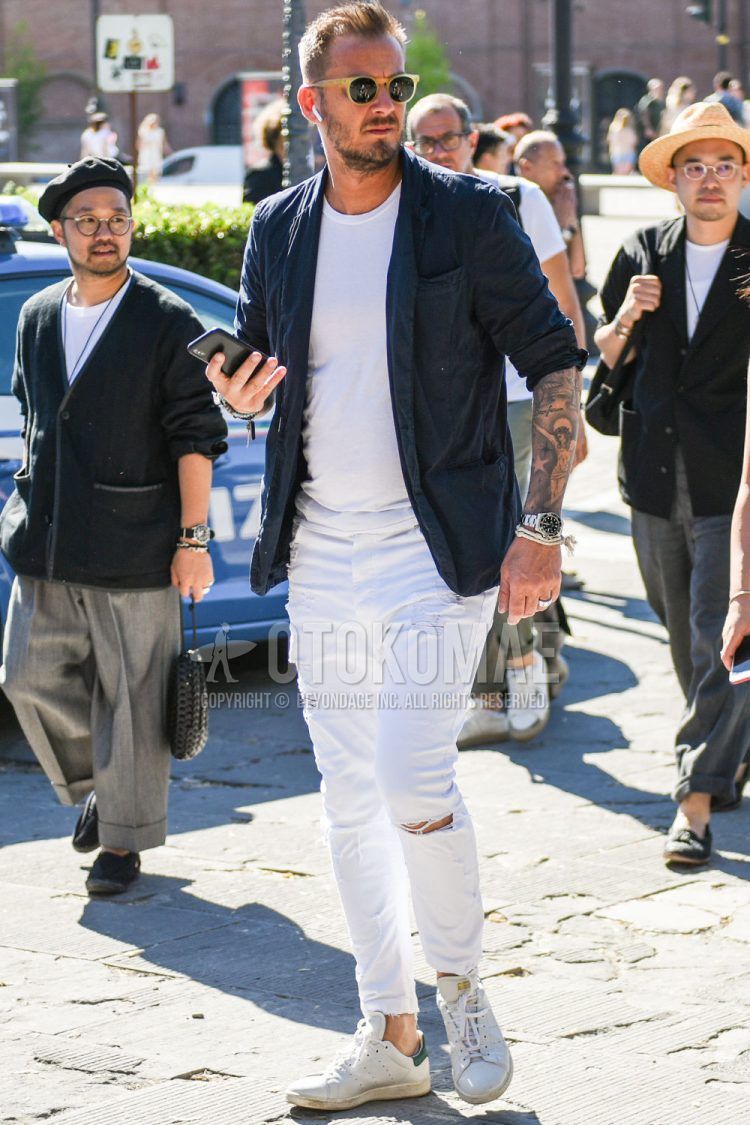 Spring, summer and fall men's coordinate outfit with plain yellow/black sunglasses, plain navy tailored jacket, plain white t-shirt, plain white damaged jeans and white low-cut sneakers.