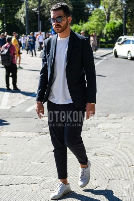 A men's spring/summer/fall outfit for men with plain black sunglasses, a plain black tailored jacket, a plain white t-shirt, plain black easy pants, and white low-cut sneakers.