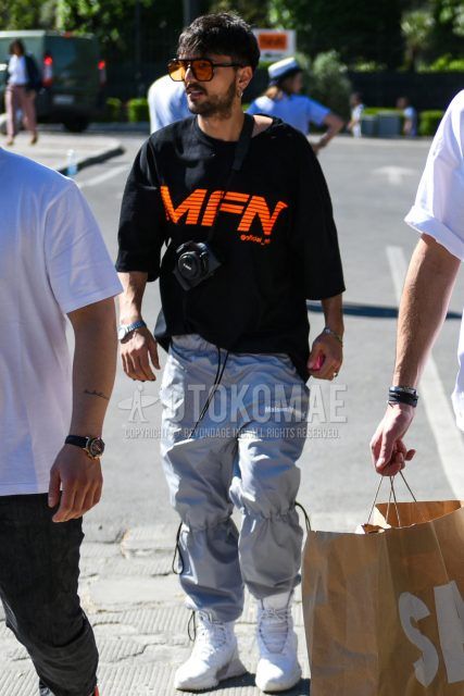 A summer men's coordinate outfit with plain black-orange sunglasses, a black graphic t-shirt, plain gray easy pants, and white high-cut sneakers.