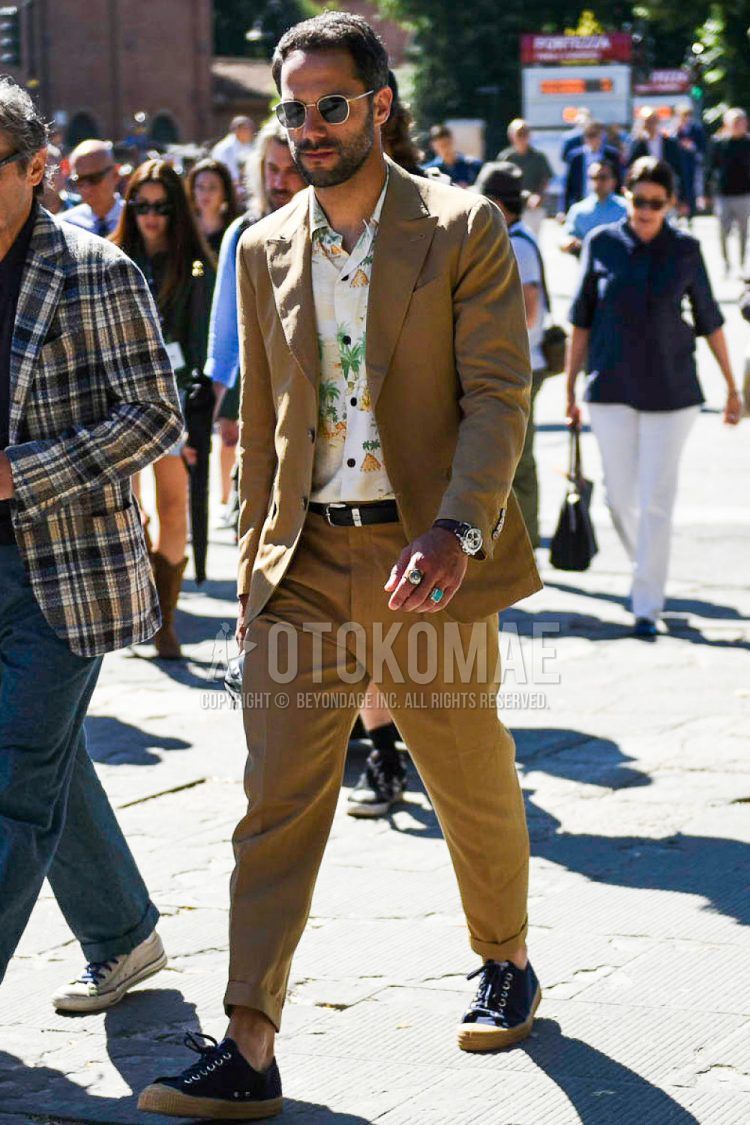 A spring, summer and fall men's coordinate outfit with round black and gold plain sunglasses, white and other shirts, a plain black leather belt, navy low-cut sneakers and a plain beige suit.