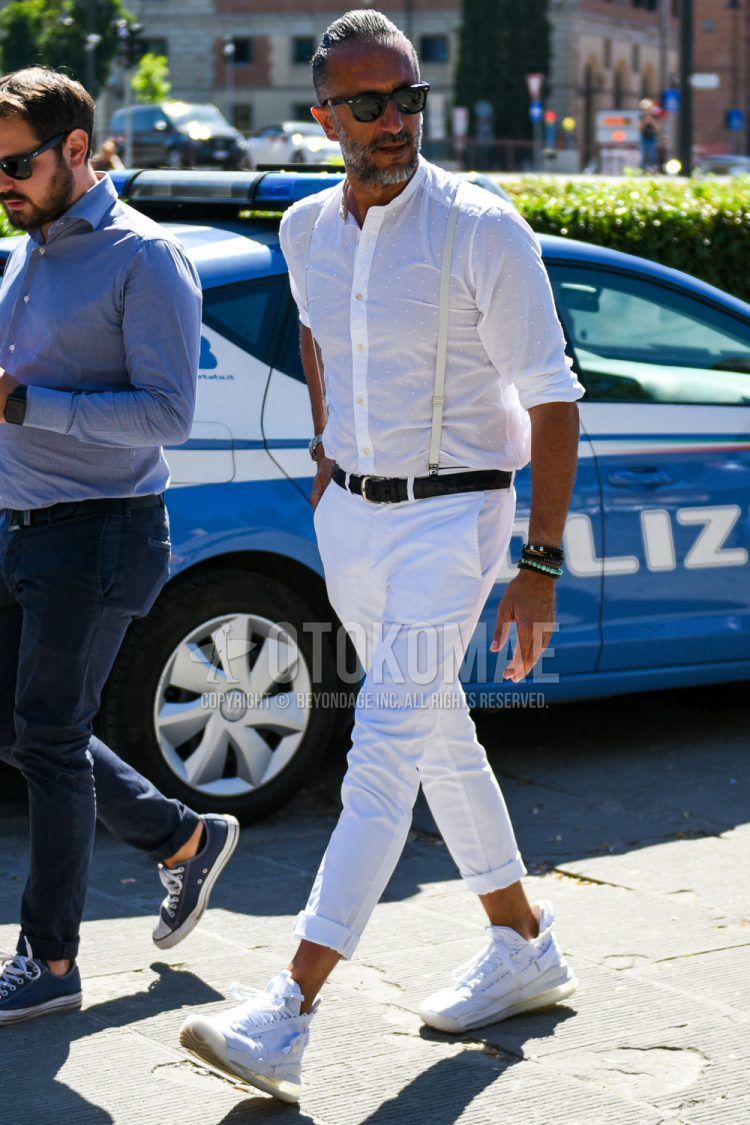 A summer/spring men's coordinate outfit with Wellington Ray-Ban Wayfarer plain black sunglasses, band collar white dotted shirt, plain black leather belt, plain white cotton pants, and white high-cut sneakers.