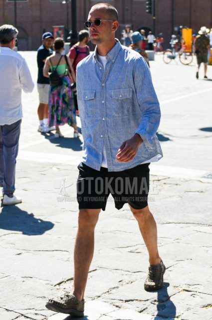 A summer men's coordinate outfit with round black and silver solid sunglasses, gray striped denim/chambray shirt, solid white t-shirt, solid black shorts, and Keen olive green sport sandals.