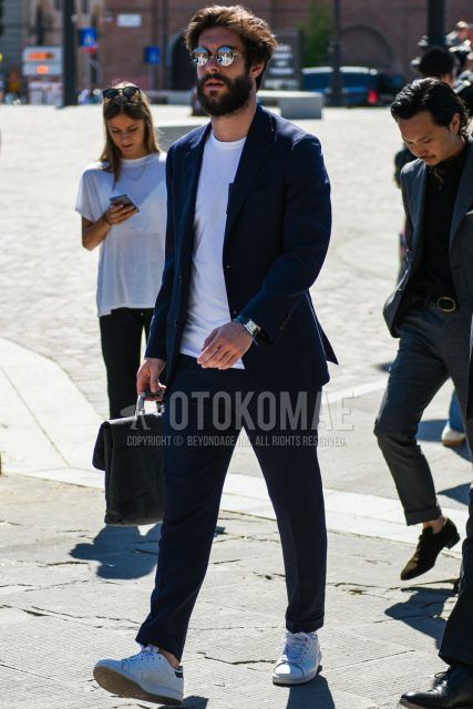 A spring, summer and fall men's coordinate outfit with round plain silver sunglasses, a plain white t-shirt, Adidas Stan Smith white low-cut sneakers and a plain navy suit.