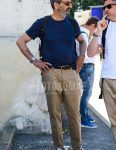 A summer men's coordinate outfit with solid beige sunglasses, solid navy t-shirt, solid brown leather belt, solid beige chinos, and Old School Vans black low-cut sneakers.